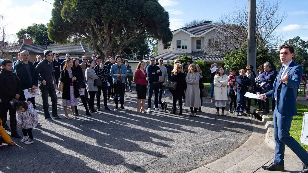 An auctioneer addressing bidders gathered for a neighborhood property sale